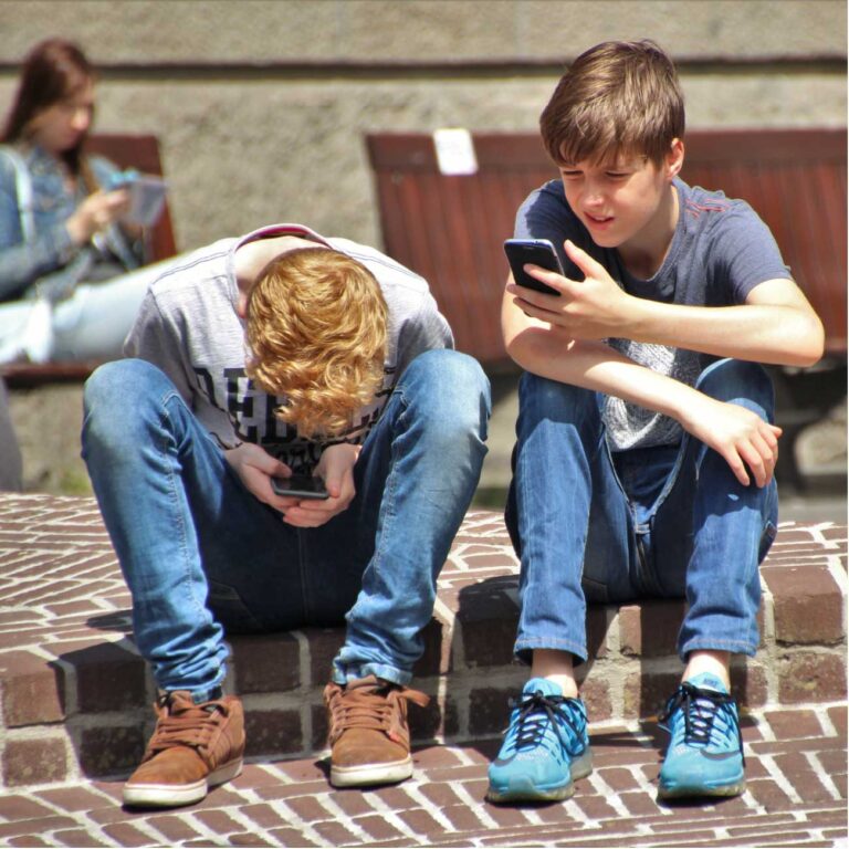 Niños sentados en las escaleras de un recinto escolar, mirando el celular