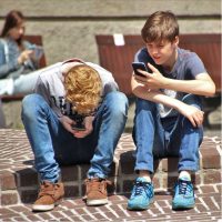 Niños sentados en las escaleras de un recinto escolar, mirando el celular